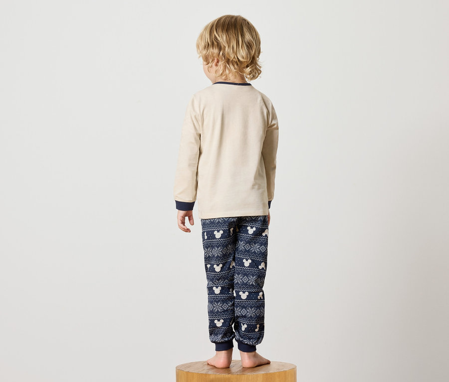 Un garçon en pyjama Mickey Mouse se tient dos à l'appareil photo sur un socle en bois.