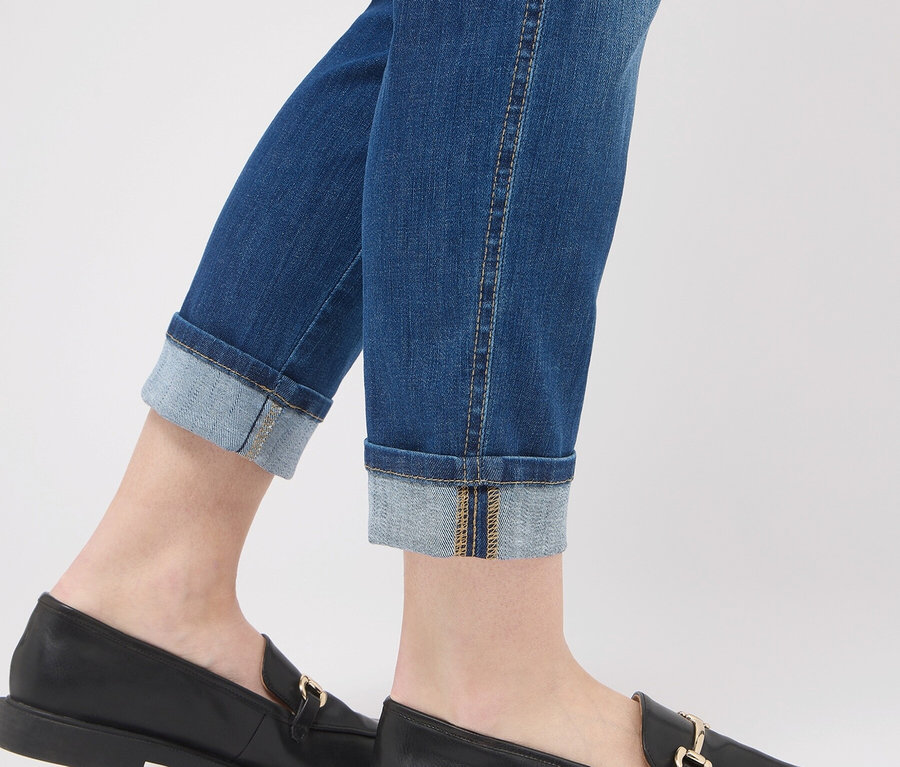 Jambes portant un jean bleu avec ourlets retroussés et des mocassins en cuir noirs avec une boucle dorée.