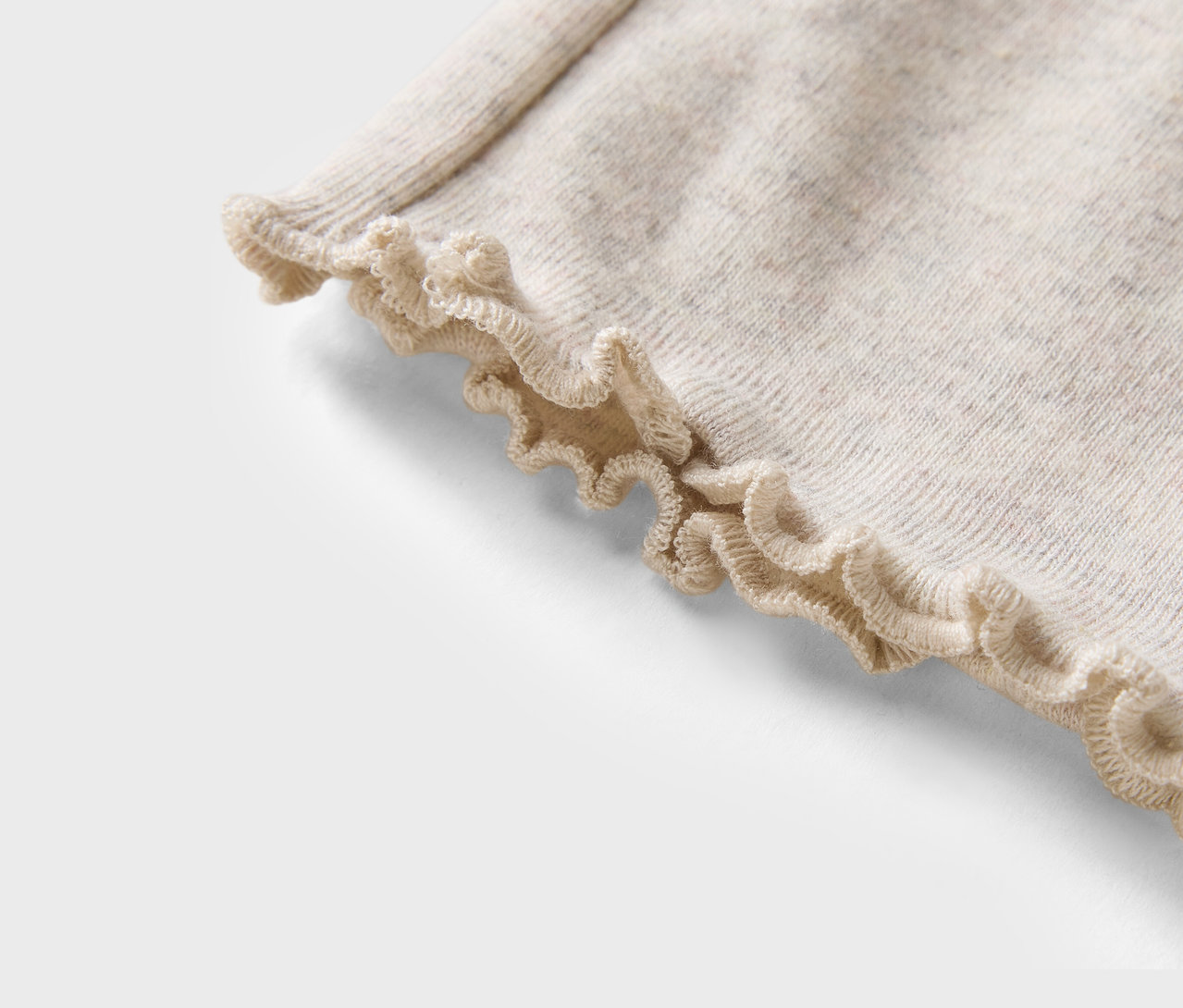 Détail d'un pull beige avec ourlet à volants.