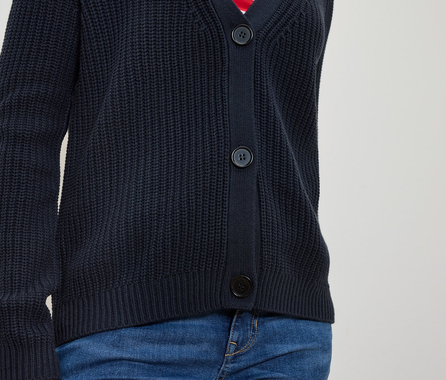 Torse d'une personne portant un cardigan en tricot bleu marine boutonné et un jean bleu.