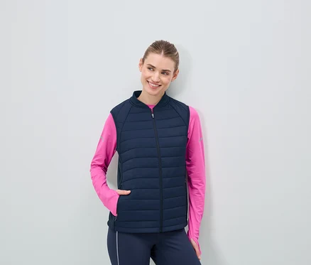 Femme portant un gilet matelassé bleu marine et un haut rose à manches longues.