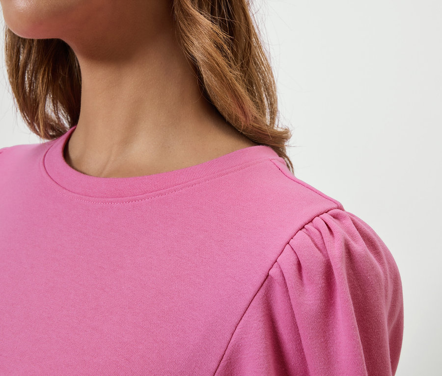 Haut du torse d'une femme portant un t-shirt rose avec des manches courtes bouffantes.