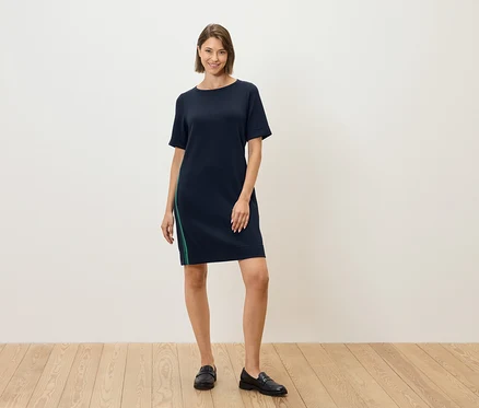 Une femme debout porte une robe bleu marine à manches courtes avec une rayure verte sur le côté.