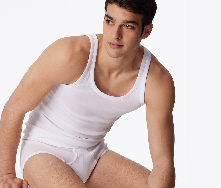 Un homme est assis sur un fond blanc et porte 2 maillots de corps blancs SCHIESSER en maille côtelée fine.