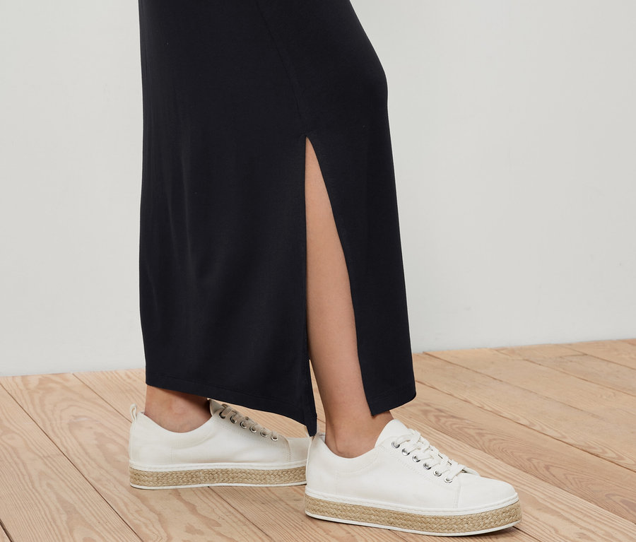 Jambes d'une femme portant une jupe longue en jersey et des chaussures en toile blanches sur un plancher en bois.