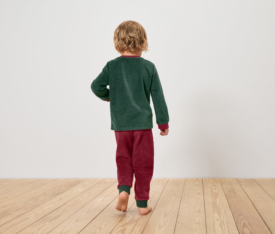 Un garçon vêtu d'un haut de pyjama vert et d'un pantalon de pyjama bordeaux marche pieds nus sur un plancher en bois.