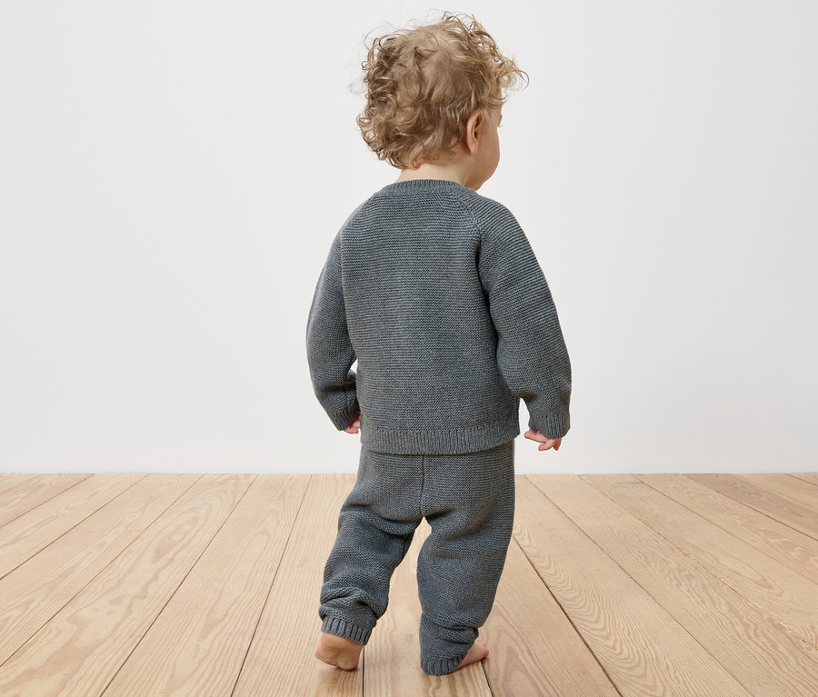 Un enfant aux cheveux bouclés porte un ensemble en maille pour bébé, vu de dos.
