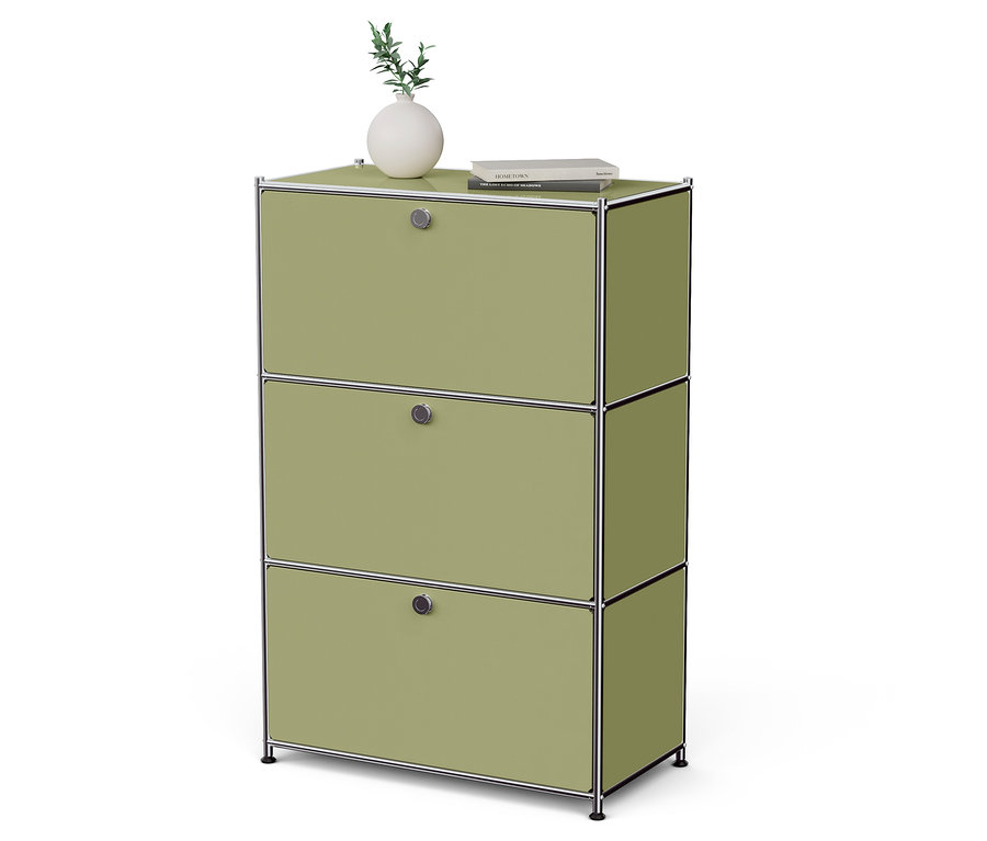 Une armoire verte avec trois tiroirs sur laquelle reposent un vase avec une plante et un livre.