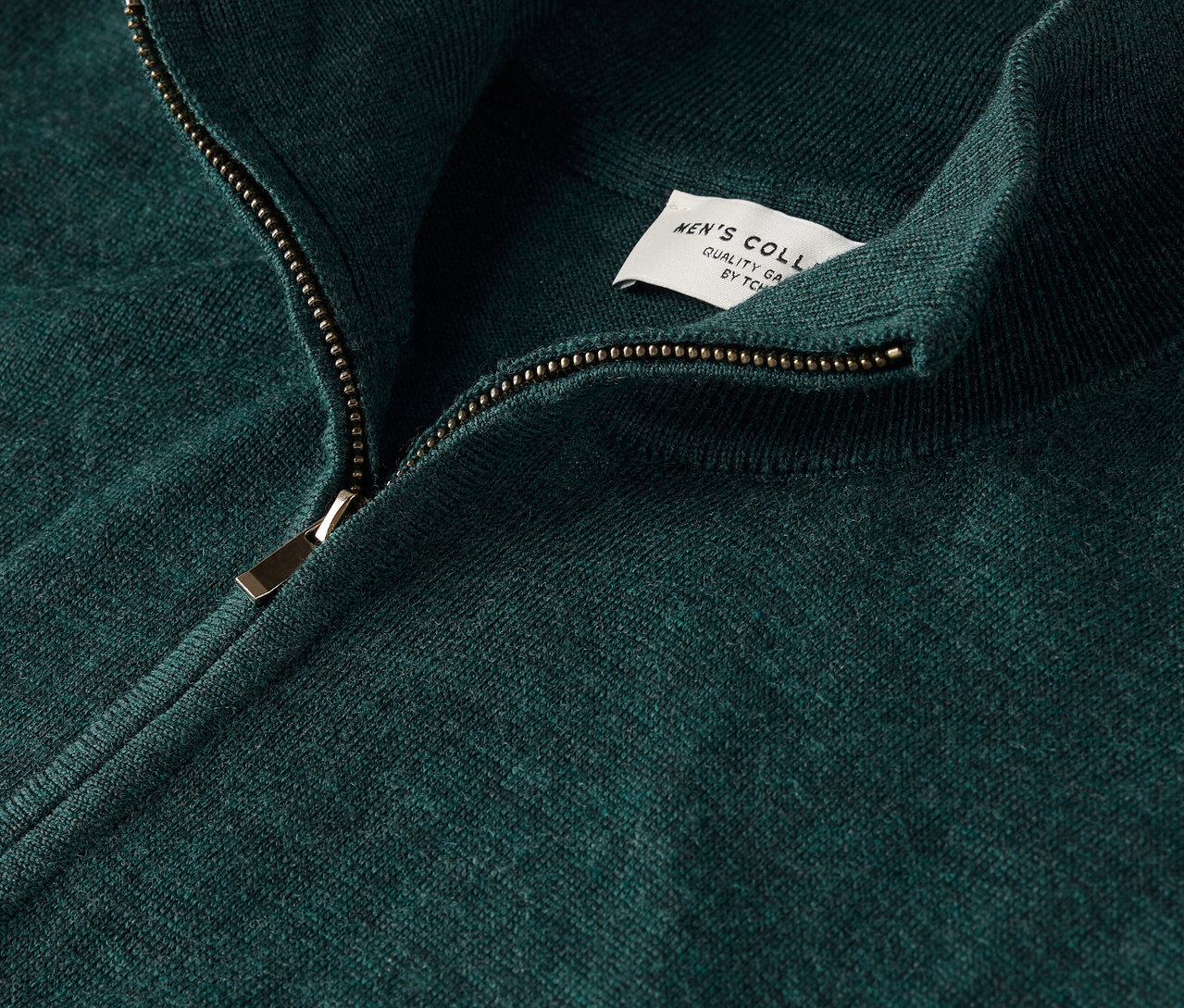 Gros plan sur un pull vert avec fermeture éclair et étiquette.