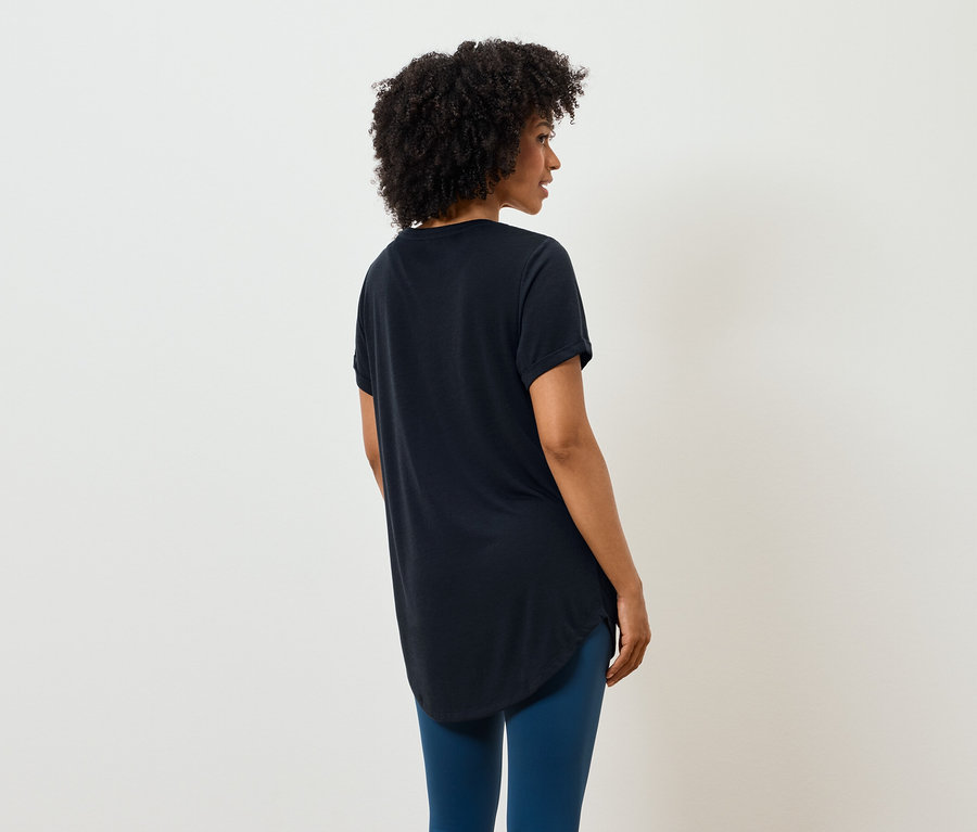Une femme avec une coiffure afro se tient dos à l'appareil photo et porte un t-shirt noir et un legging bleu.