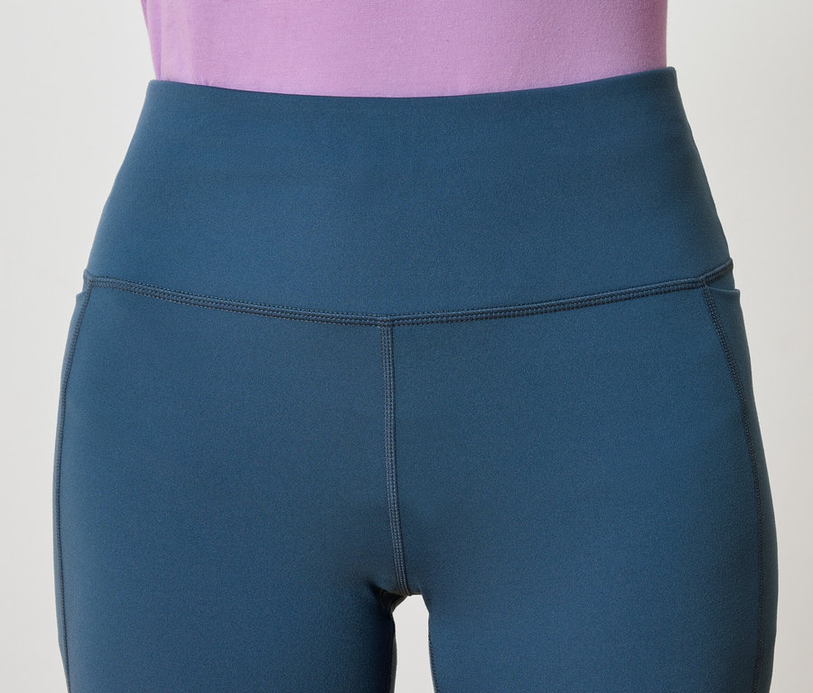 Gros plan sur un legging bleu taille haute avec une poche, porté avec un haut violet.