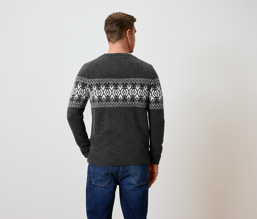 Un homme, vu de dos, porte un pull gris à motifs et un jean bleu.