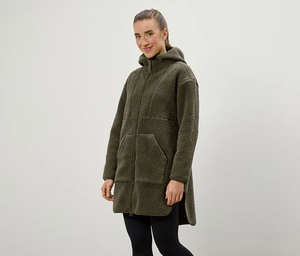 Une femme porte un manteau à capuche vert olive et un legging noir.