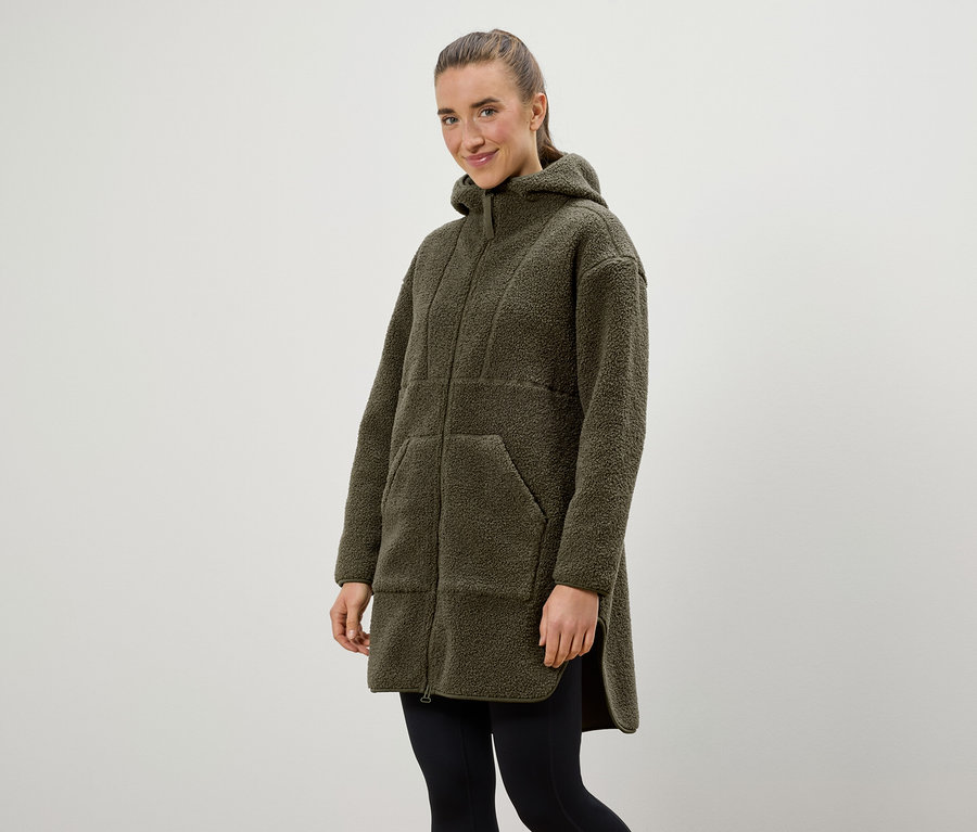 Une femme porte un manteau à capuche vert olive et un legging noir.