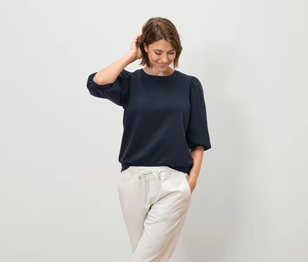 Femme posant dans un chemisier bleu marine à manches courtes et un pantalon clair.