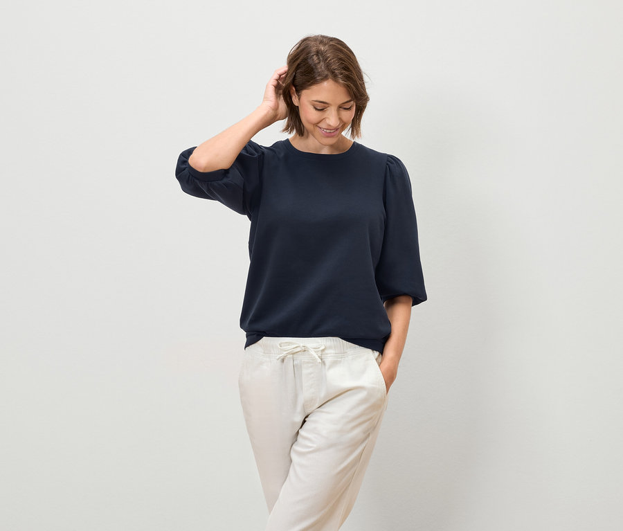 Femme posant dans un chemisier bleu marine à manches courtes et un pantalon clair.