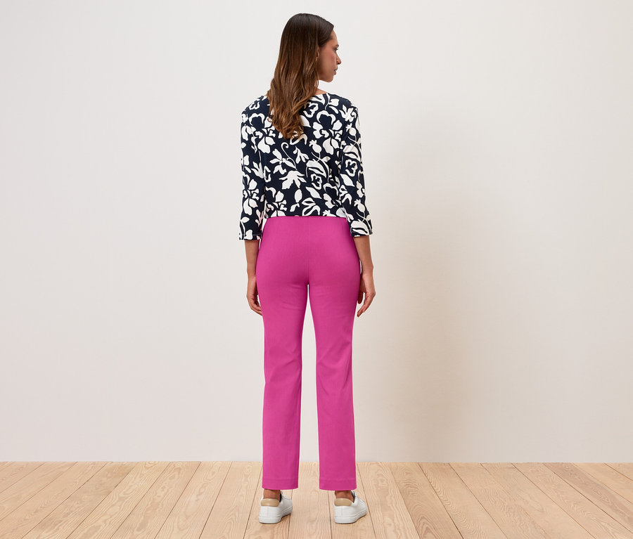 Une femme, vue de dos, porte un chemisier à fleurs et un pantalon rose.
