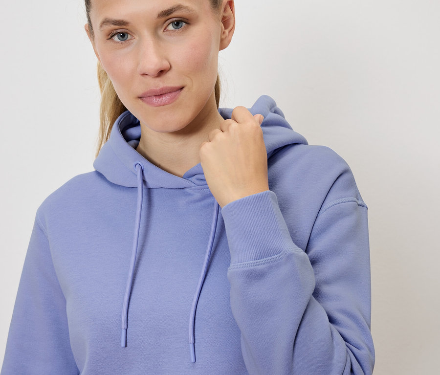 Portrait d'une femme blonde portant un sweat à capuche lilas, tenant sa capuche.