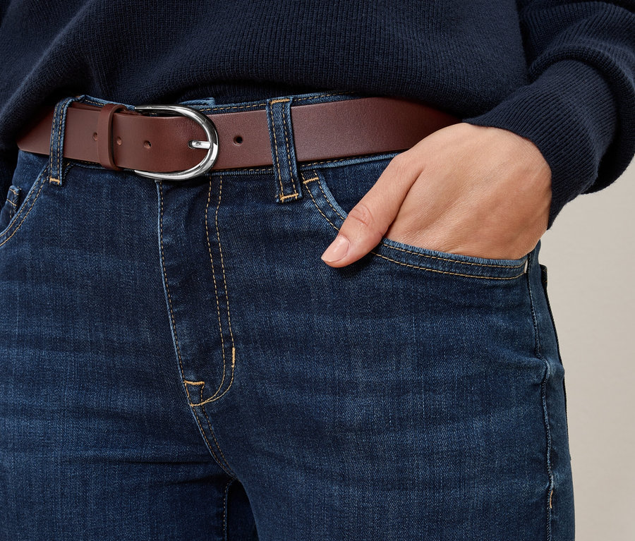 Gros plan sur un jean bleu avec une ceinture en cuir cognac.
