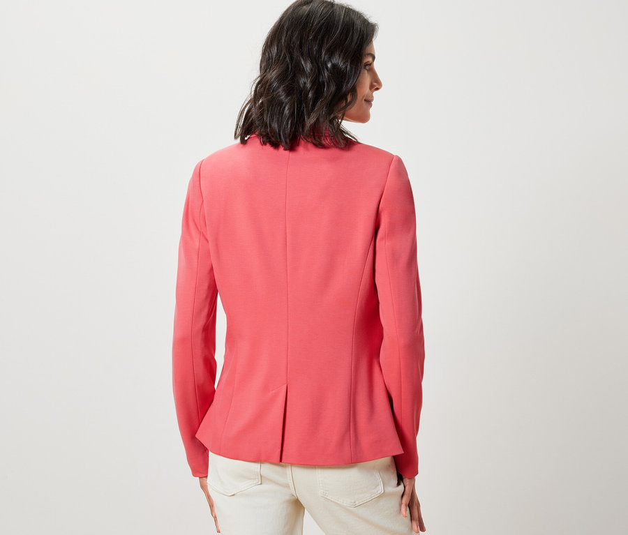 Une femme, vue de dos, porte un blazer en jersey corail et un pantalon clair.