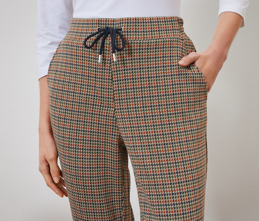 Détail d'un pantalon pour femme à motif pied-de-poule avec une main dans la poche.