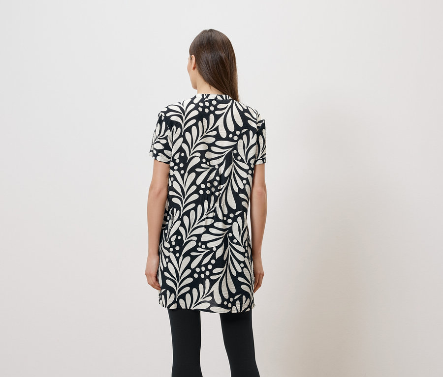 Vue arrière d'une femme aux longs cheveux bruns portant une robe à manches courtes noire et blanche à motifs de feuilles et des leggings noirs.