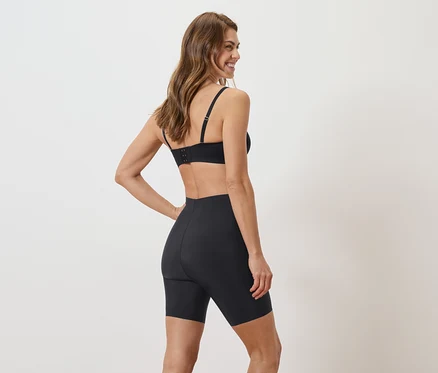 Une femme se tient dos à la caméra, portant un soutien-gorge et un short noirs.