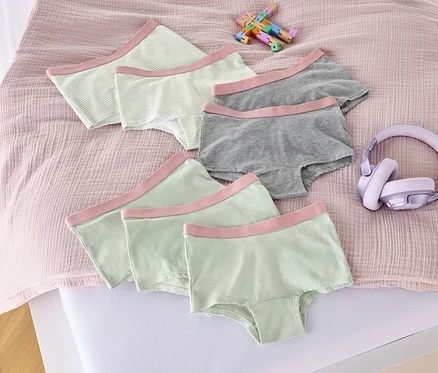 Sur un lit sont disposés sept culottes pour filles rose fané, un jouet et un casque audio.