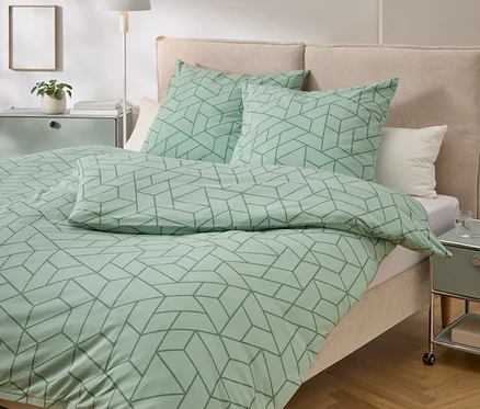 Lit avec des draps vert menthe à motif géométrique, deux oreillers, une table de chevet et une lampe.