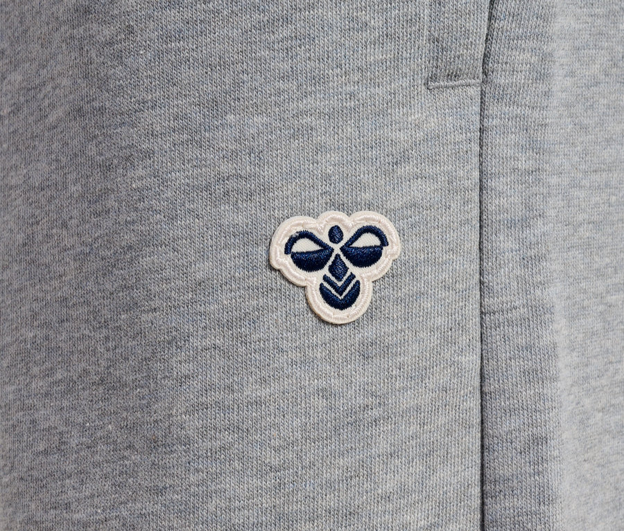 Gros plan sur un pantalon de jogging gris avec un petit logo brodé.
