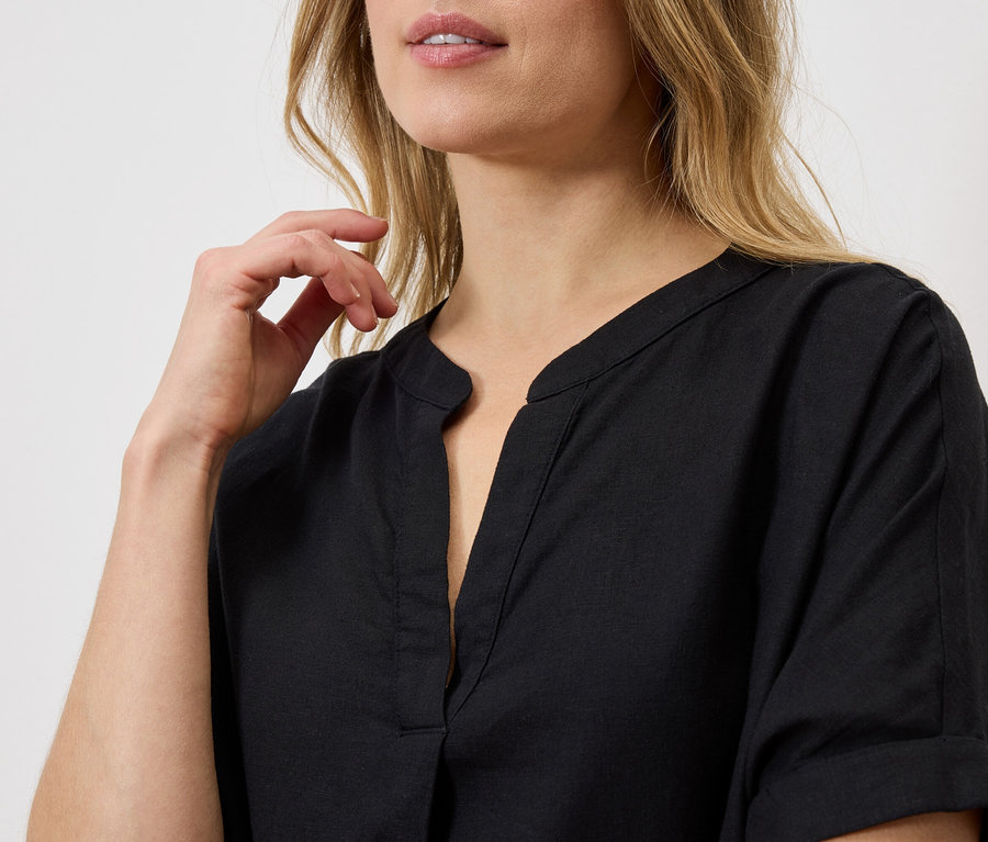 Gros plan d'une femme blonde portant une chemise noire boutonnée et tenant sa main près de son visage.