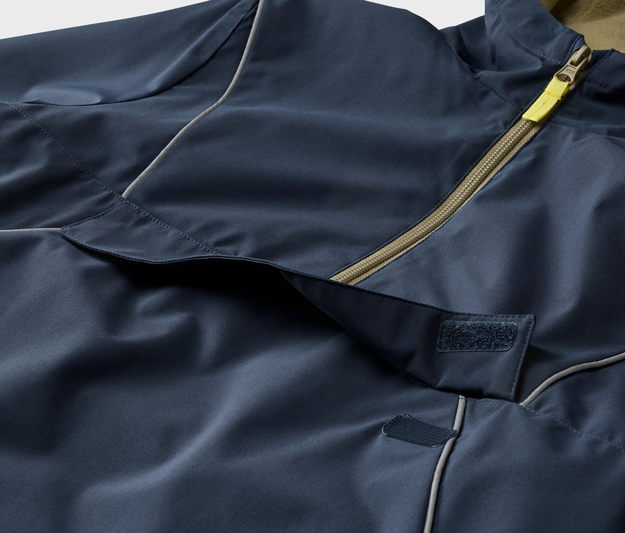 Gros plan d'une veste bleu marine avec fermeture éclair jaune et velcro.