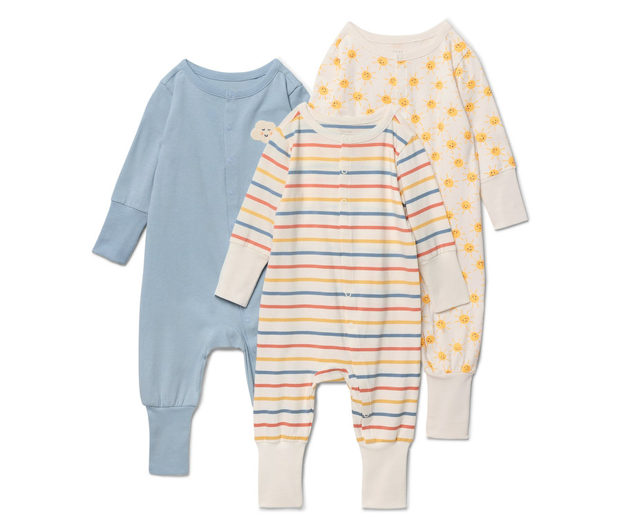 Trois pyjamas pour bébé sont posés sur un fond blanc. Le pyjama de gauche est bleu avec un petit nuage sur la poitrine. Le pyjama du milieu est rayé beige, jaune, rouge et bleu. Le pyjama de droite est crème avec un motif de soleil jaune.