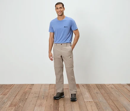 Un homme debout portant un t-shirt bleu, un pantalon beige et des chaussures marron.