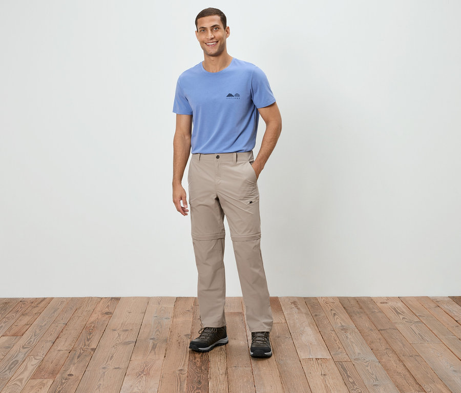 Un homme debout portant un t-shirt bleu, un pantalon beige et des chaussures marron.