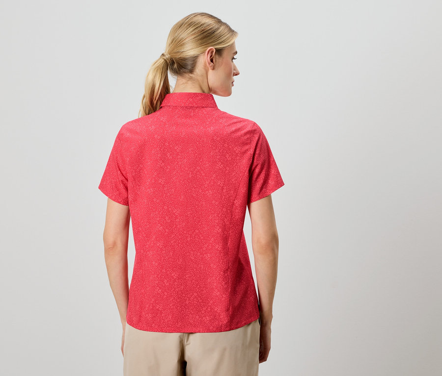 Vue arrière d'une femme blonde portant une chemise rouge à manches courtes et un pantalon beige.