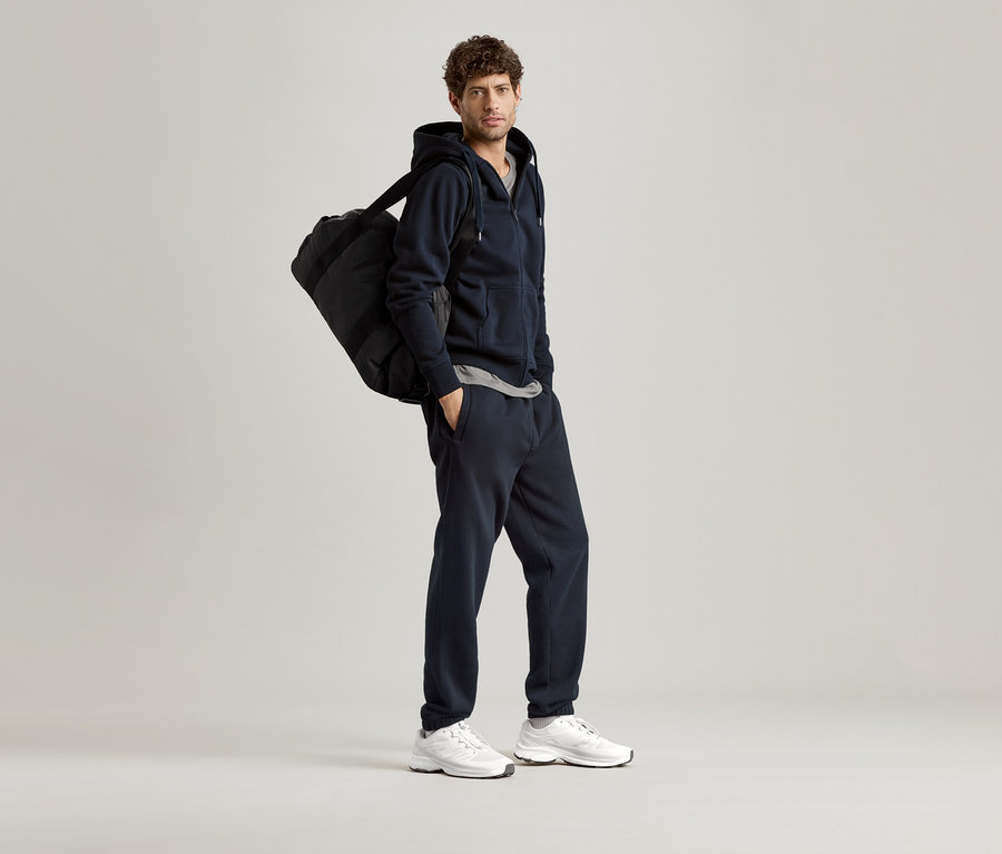 Homme portant un sweat à capuche bleu marine avec un sac de sport sur l'épaule.