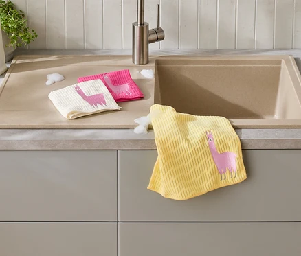 Trois chiffons à vaisselle avec un motif de lama sont posés sur un comptoir de cuisine à côté d'un évier.