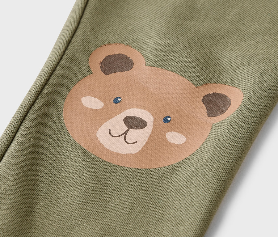 Gros plan d'un pantalon vert olive avec une tête d'ours marron sur la jambe.