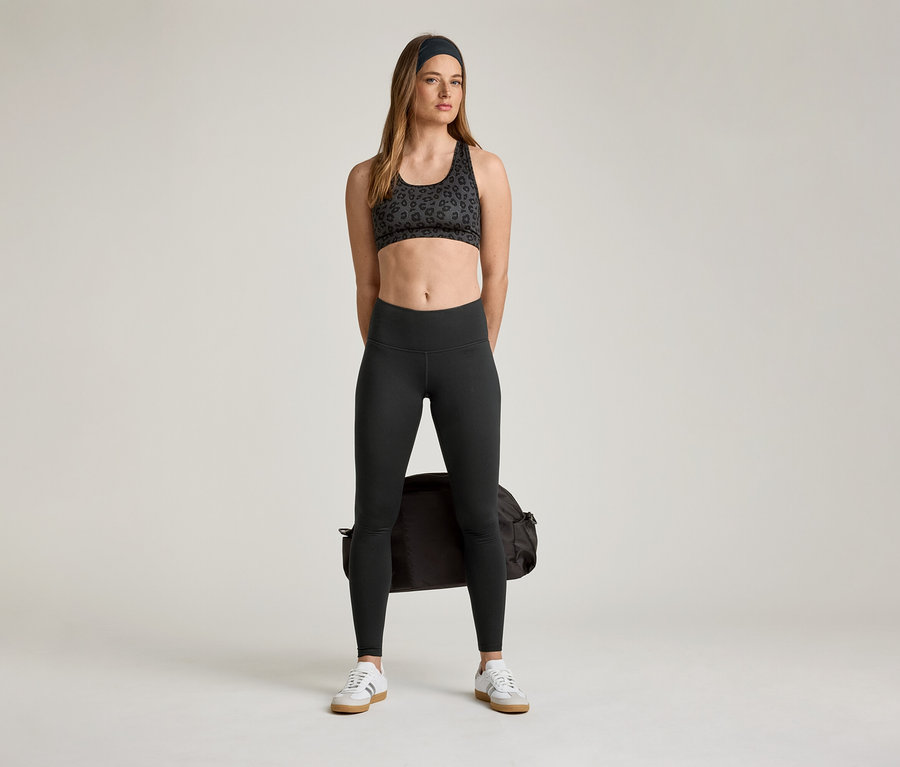 Femme portant une brassière de sport et un legging de sport « ActiveSoft » avec un sac de sport et des baskets.