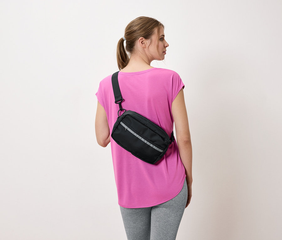 Femme vue de dos avec un sac bandoulière noir, un t-shirt rose et un legging gris.