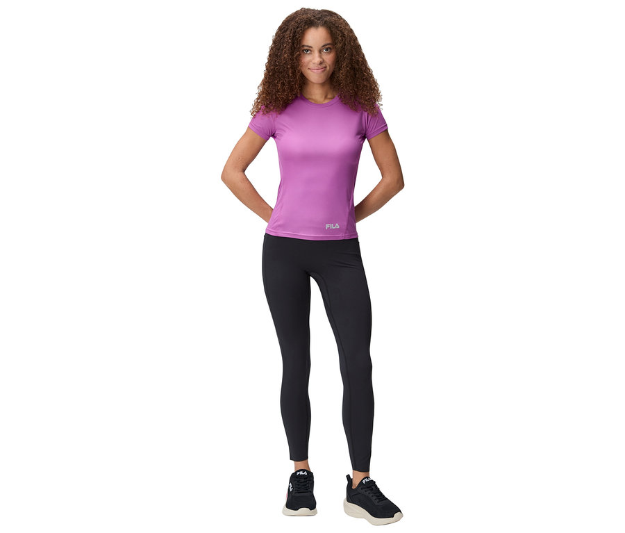 Femme debout, les mains derrière le dos, portant un t-shirt violet, un legging noir et des baskets.