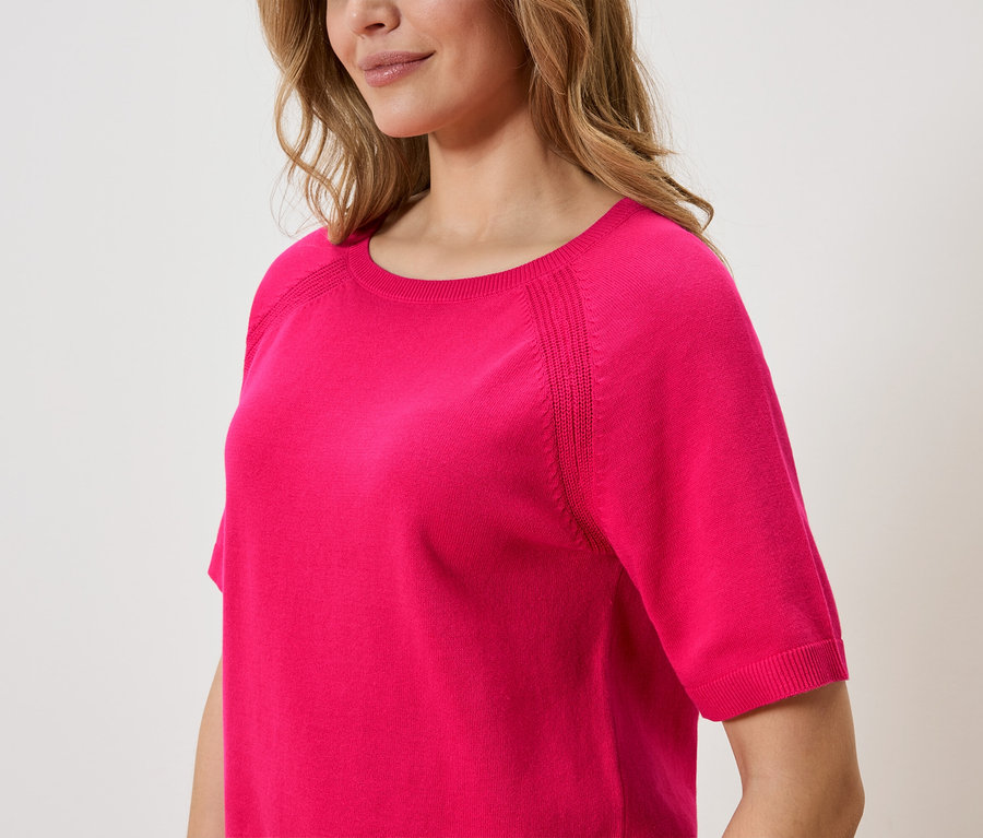 Une femme porte un pull rose à manches courtes.