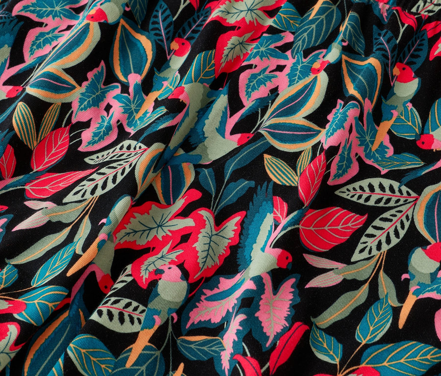 Gros plan d'un tissu à motif tropical avec des feuilles et des perroquets bleus, roses, verts et rouges sur fond noir.