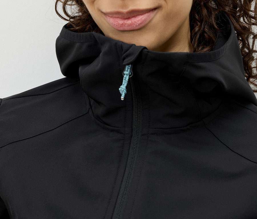 Gros plan d'une femme aux cheveux bouclés portant une veste à capuche noire avec une fermeture éclair bleue.