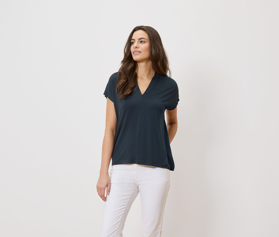 Une femme porte un t-shirt bleu marine et un pantalon blanc sur un fond blanc.