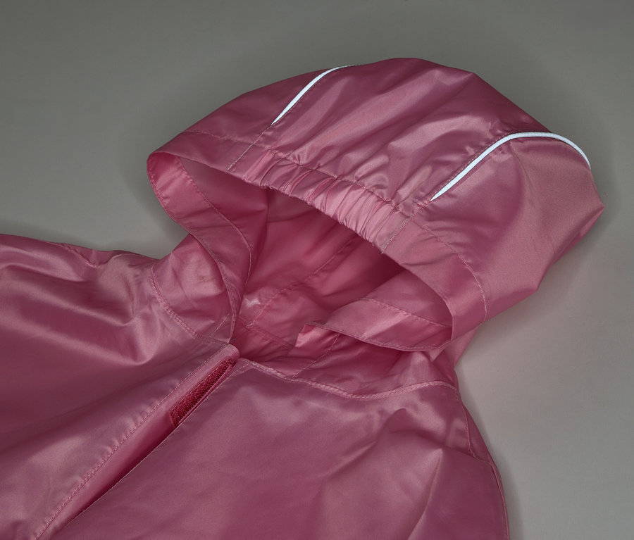 Gros plan d'une veste rose à capuche avec des détails blancs sur fond gris.