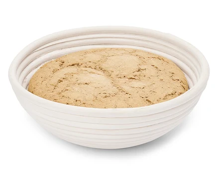 Une miche de pâte repose dans un banneton rond blanc.