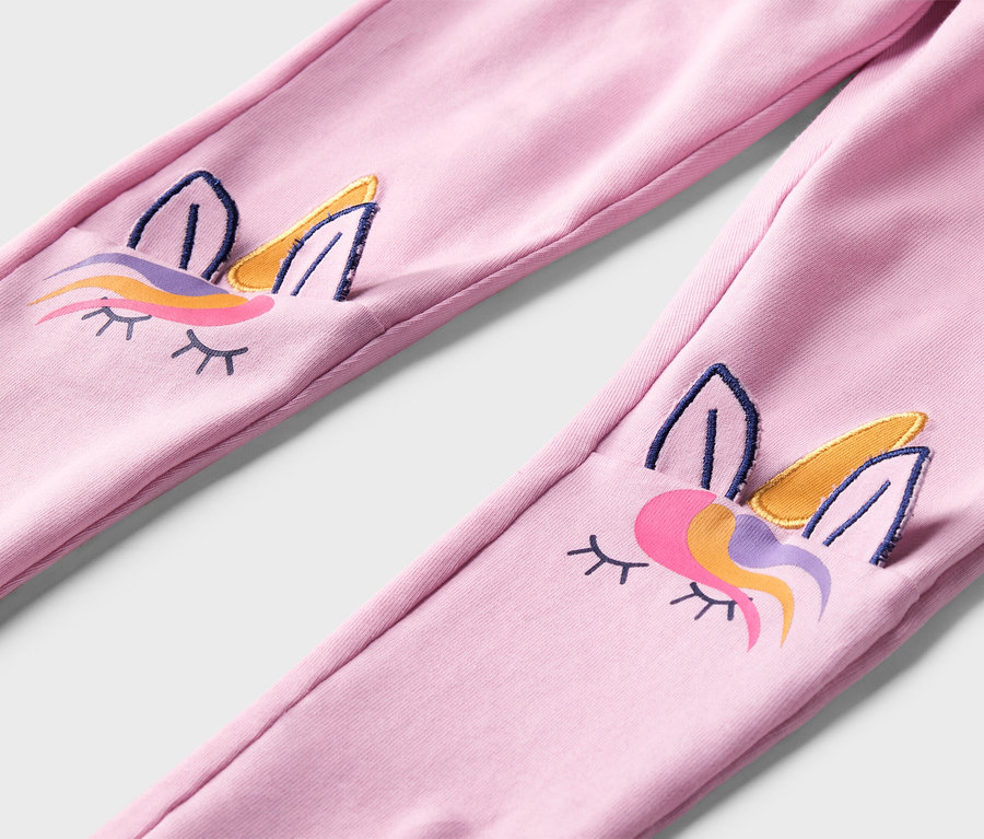 Gros plan sur un legging rose avec des visages de licorne brodés aux genoux.