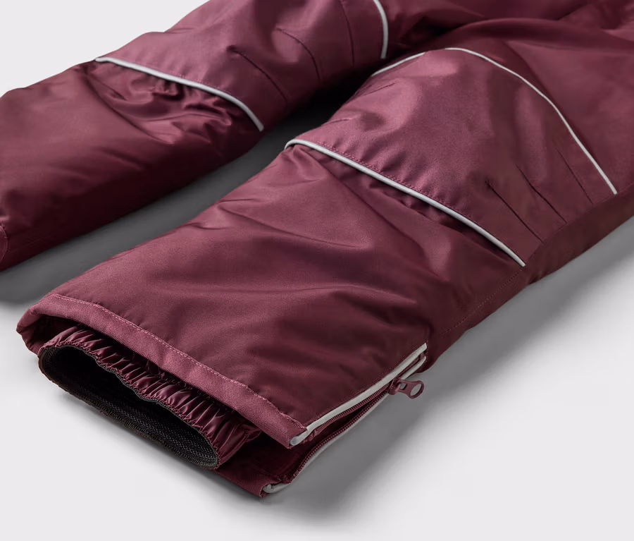 Gros plan sur un pantalon bordeaux avec passepoil blanc et fermeture éclair en bas de jambe.